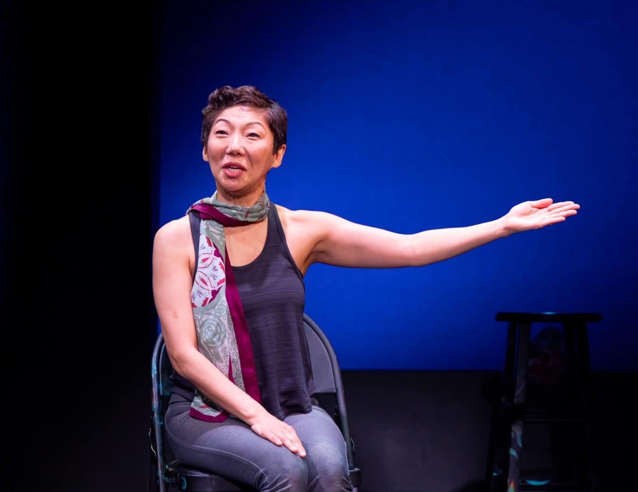 Sun Mee Chomet sits in a chair while performing How to Be A Korean Woman
