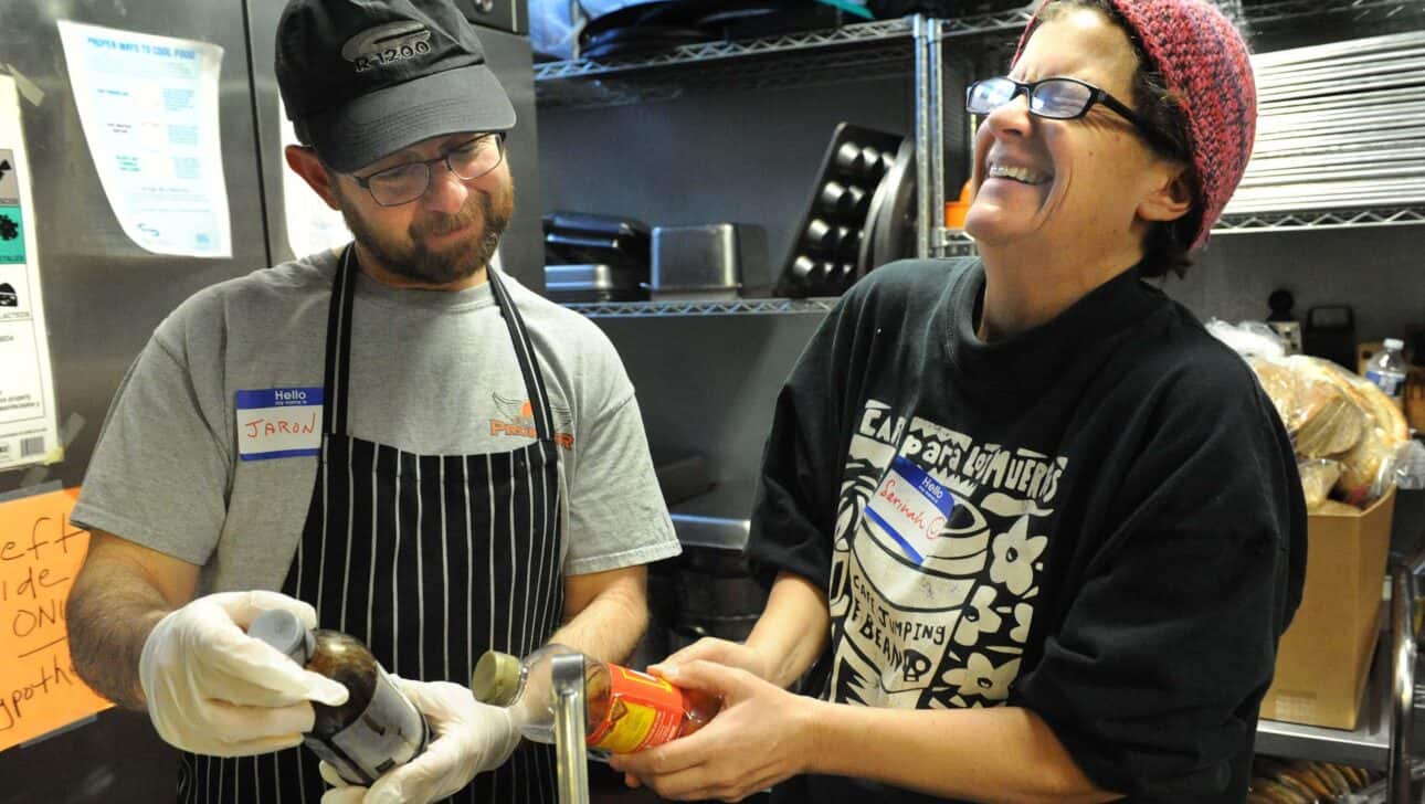 two volunteer cooks laughing in a kitchen.