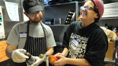 two volunteer cooks laughing in a kitchen.