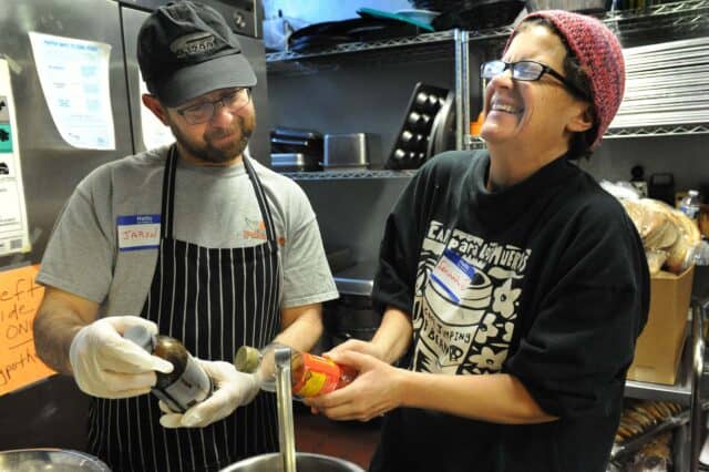 two volunteer cooks laughing in a kitchen.