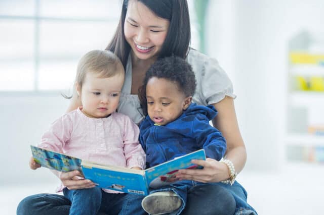 Photo of nanny reading a book to two toddlers