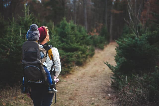 Photo of woman walking along path with baby carrier on back.