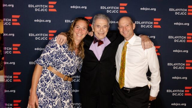 Photo of one woman and two men dressed in formal wear posing in front of a navy blue backdrop with the Edlavitch DCJCC logo.